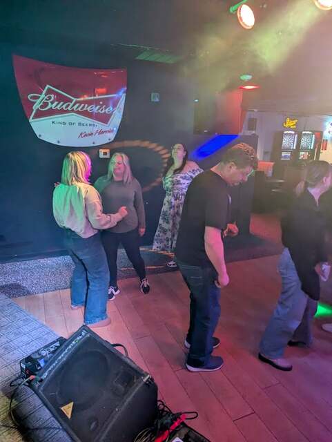 Group dancing near the Budweiser sign at a bar karaoke event